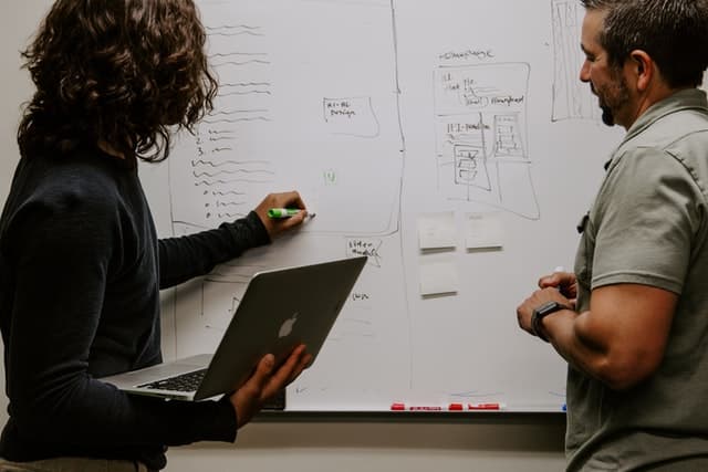 Two men discussing and writing in a whiteboard